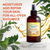 Bottle of 'Gustavine' Anti-Aging Body Treatment with green leaves and gold liquid splash in the background.