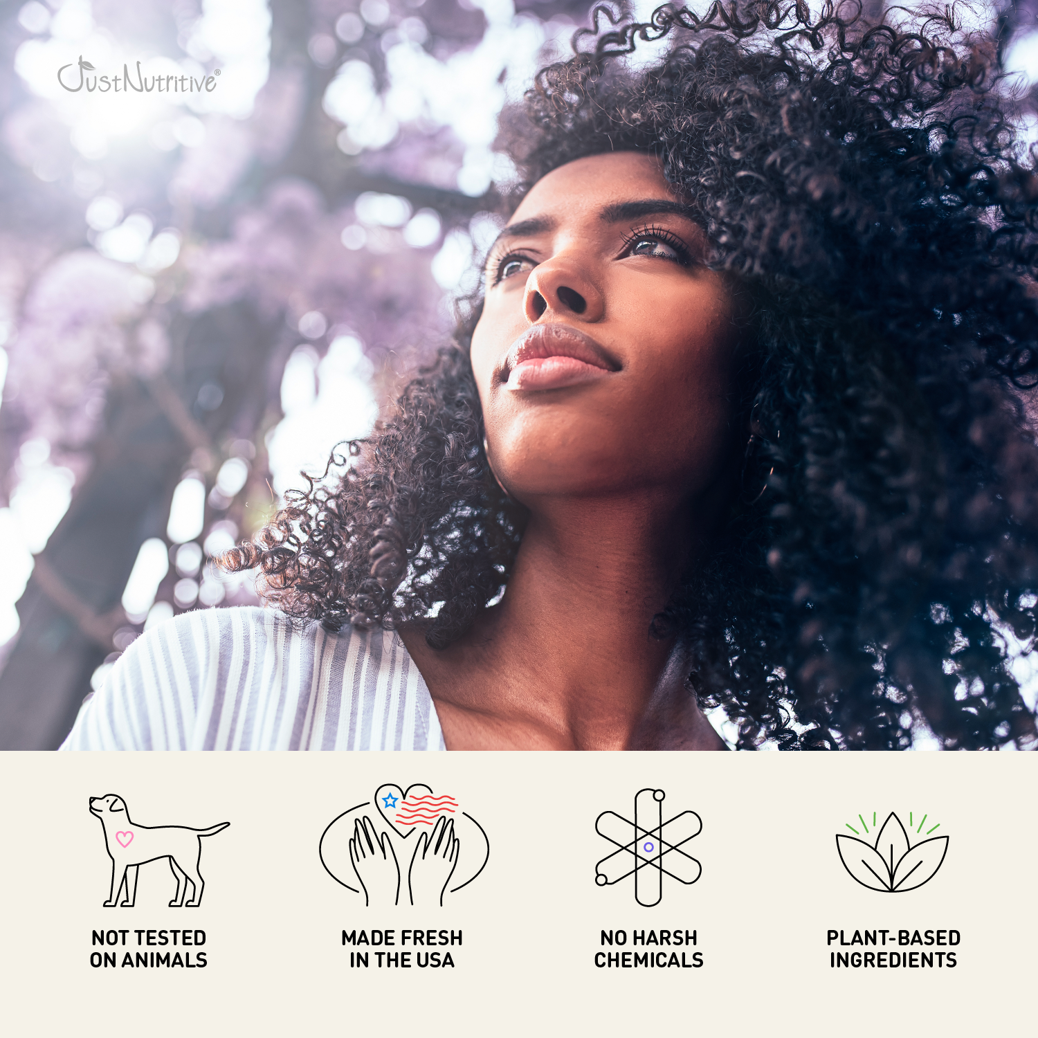 Woman with natural hair standing outdoors with cherry blossoms, featuring JustNaturals brand icons and claims.